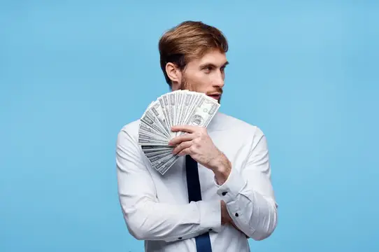 Молодой мужчина в белой рубашке держит веер из долларов на голубом фоне