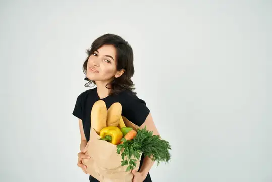 Женщина с бумажным пакетом продуктов в руках доставляет овощи для здорового питания