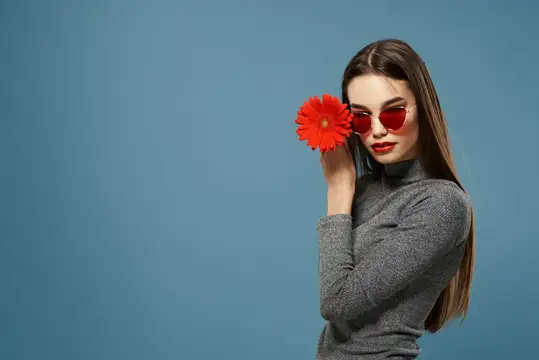 Девушка в красных очках с цветком у лица на синем фоне