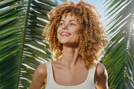 Улыбающаяся кудрявая девушка на фоне пальмовых листьев