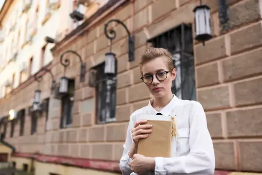 Светловолосая девушка в очках с книгой на фоне старинного здания