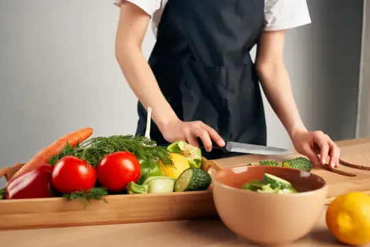 Повар в чёрном фартуке нарезает свежие овощи на кухне