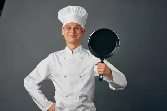 Улыбающийся повар в белом колпаке держит сковороду