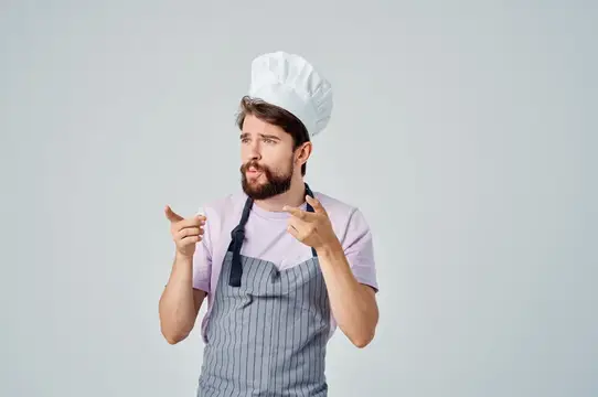 Бородатый мужчина в поварском колпаке и фартуке жестикулирует руками
