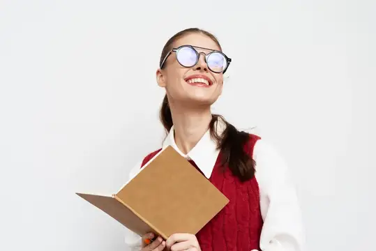 Улыбающаяся девушка в очках с книгой мечтательно смотрит вверх
