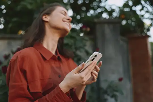 Улыбающаяся девушка с телефоном в руках на фоне зелени