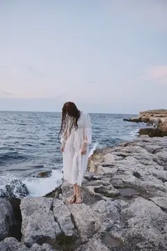 Девушка в белом платье стоит на камнях у моря