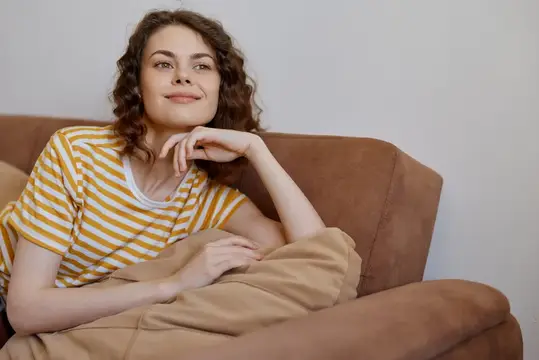 Кудрявая девушка в полосатой футболке отдыхает на диване