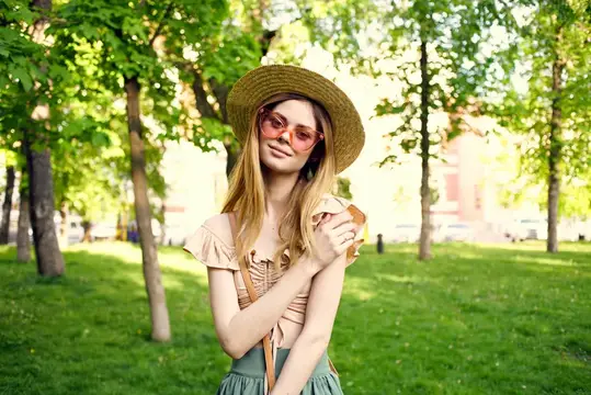 Молодая блондинка в соломенной шляпе и розовых очках гуляет по летнему парку