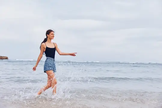 Молодая женщина весело бежит по воде у морского берега