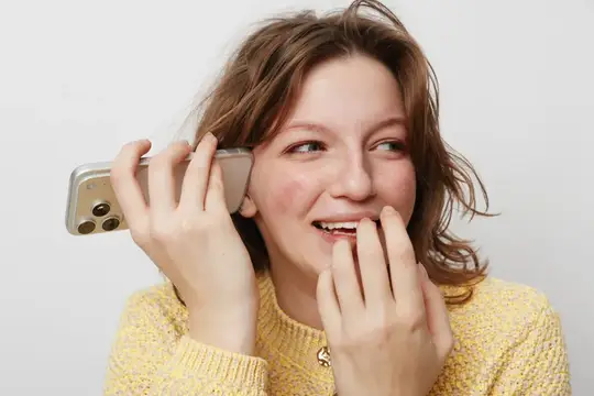 Улыбающаяся молодая женщина с каштановыми волосами и естественной кожей держит смартфон у уха