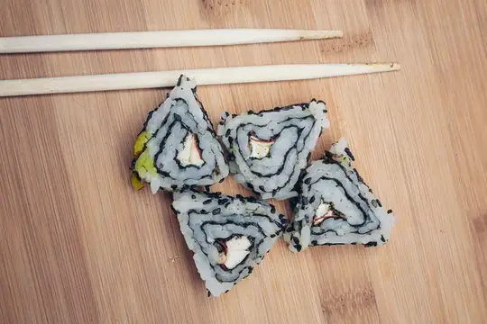 Роллы с белым рисом и палочки на бамбуковой доске