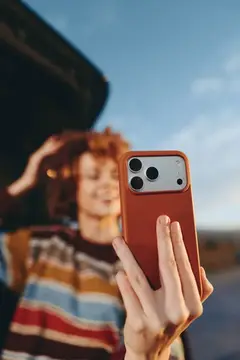 Рыжеволосая девушка фотографирует на смартфон в оранжевом чехле