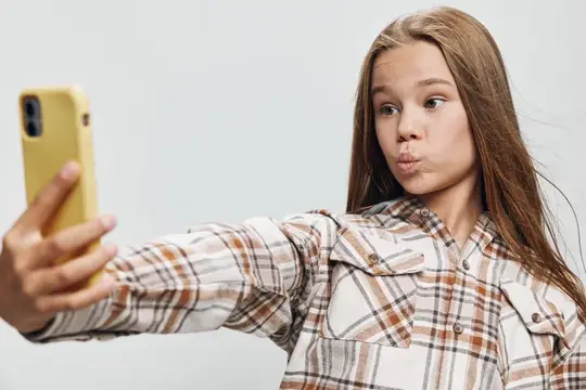 Юная девушка в клетчатой рубашке делает селфи на мобильный телефон