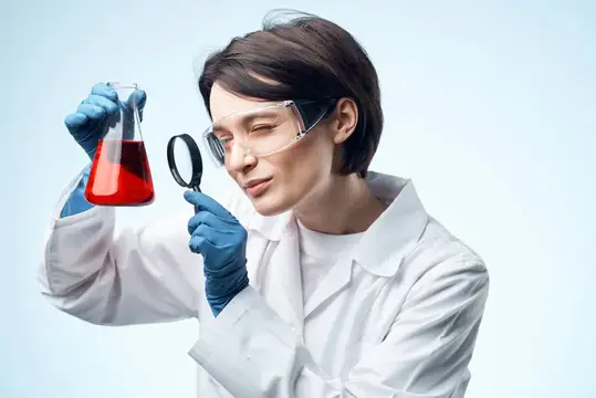 Женщина-учёный рассматривает химический раствор через увеличительное стекло, занимаясь биотехнологическими исследованиями