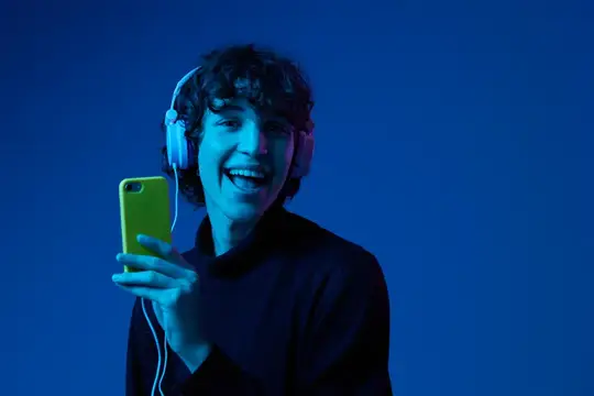 Улыбающийся парень в наушниках смотрит в смартфон в синем свете