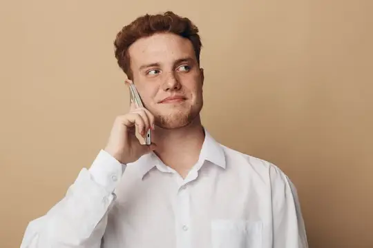 Портрет молодого мужчины в белой рубашке, использующего смартфон, со спокойным выражением лица, смотрящего в сторону