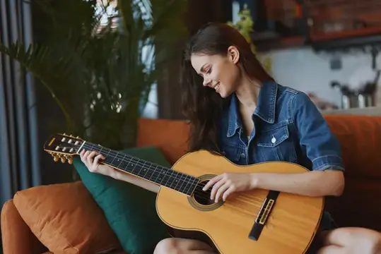 Улыбающаяся темноволосая девушка играет на акустической гитаре дома