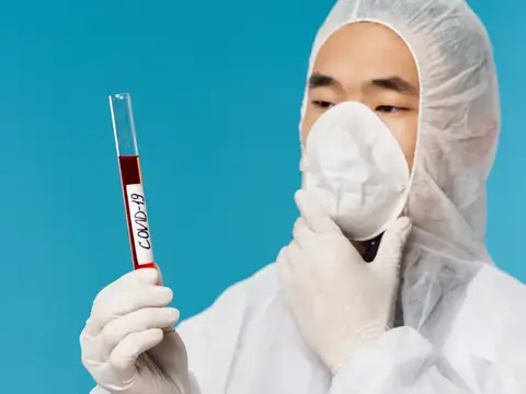 Мужчина в защитном костюме держит пробирку с анализом на COVID-19