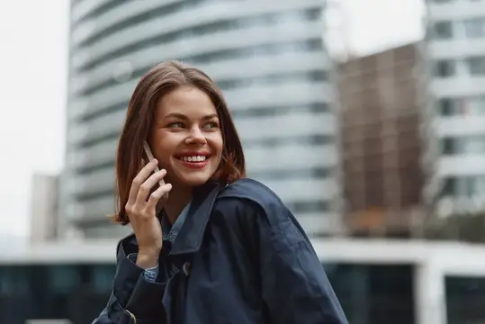 Улыбающаяся девушка говорит по телефону на фоне офисных зданий