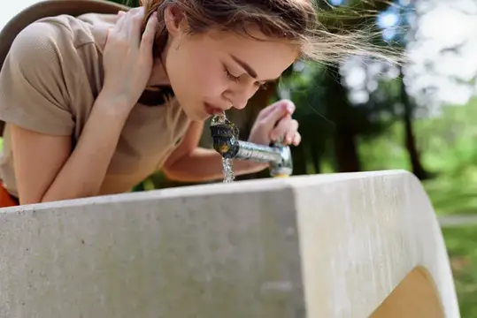 Девушка пьёт воду из уличного крана в парке