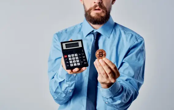 Бородатый мужчина в рубашке с калькулятором и биткоином