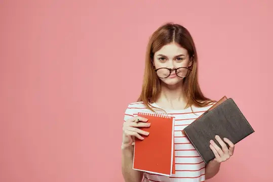 Красивая студентка держит книги, жестикулирует руками на розовом фоне