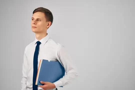 Молодой человек в белой рубашке с синей папкой на сером фоне