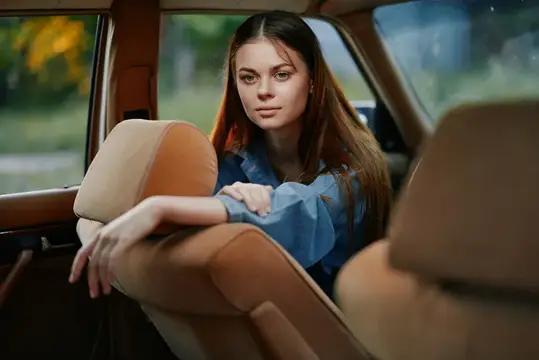 Молодая шатенка в голубой блузке сидит на заднем сиденье автомобиля