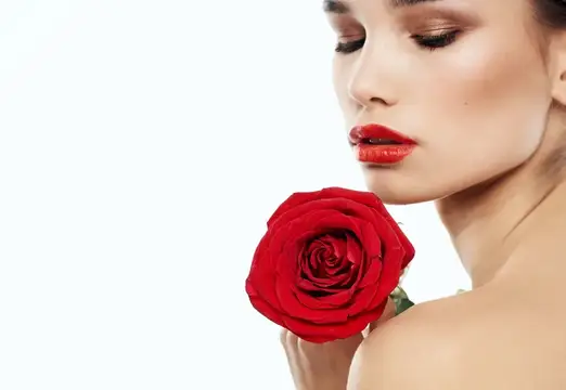 Красивая женщина с красной розой у лица на белом фоне