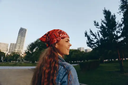 Улыбающаяся девушка в красной бандане на фоне городского парка