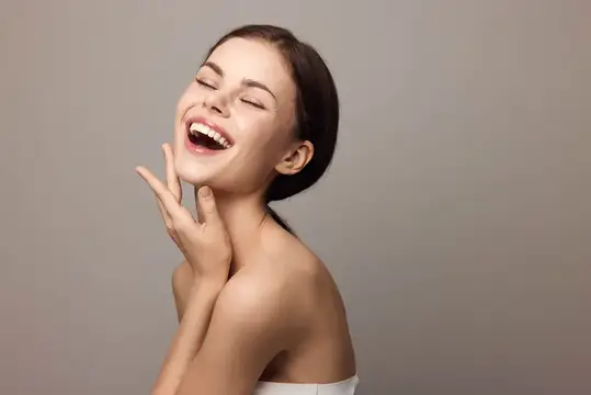 Смеющаяся молодая женщина с закрытыми глазами на сером фоне