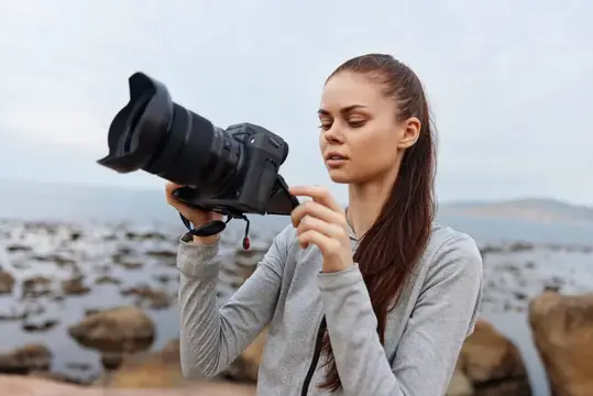 Молодая женщина настраивает фотокамеру на каменистом берегу
