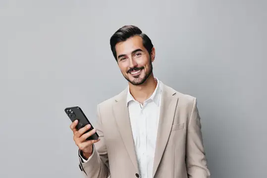 Улыбающийся мужчина в бежевом пиджаке держит смартфон