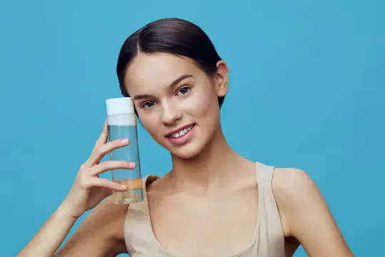 Молодая девушка с прозрачным флаконом косметики на голубом фоне