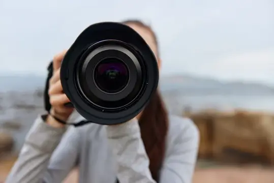 Девушка фотограф смотрит в объектив камеры на природе