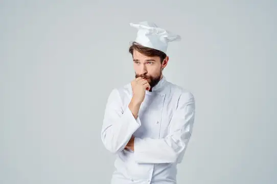 Задумчивый бородатый повар в белом колпаке на сером фоне