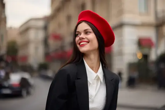 Модная женщина улыбается, показывая зубы, стоя на улице на фоне города