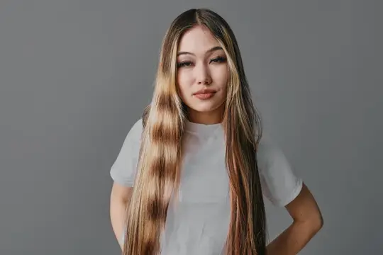 Азиатская девушка с длинными светлыми волосами на сером фоне
