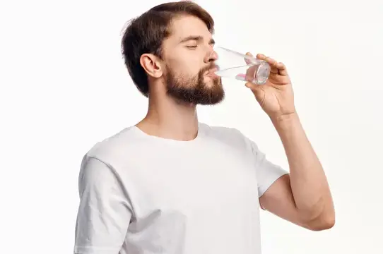 Молодой бородатый мужчина пьёт воду из стакана