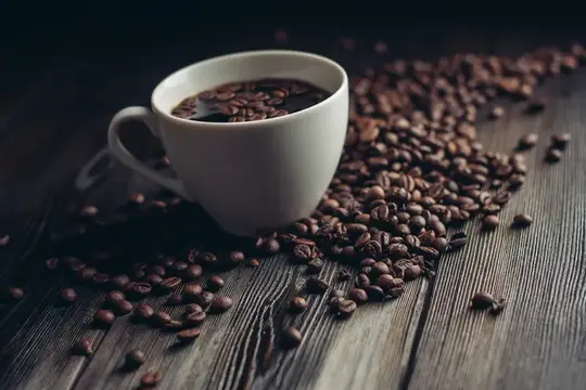Белая чашка кофе и рассыпанные зерна на темном деревянном столе