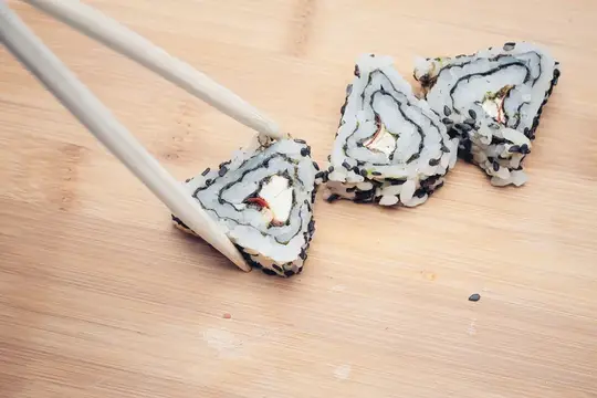 Палочки подхватывают кусочек ролла с лососем на деревянной доске