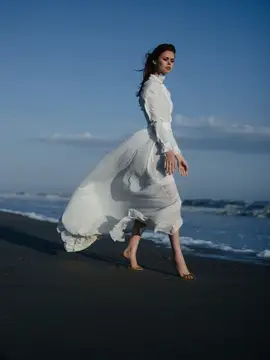 Женщина в белом платье идет по пляжу вдоль океана во время отпуска