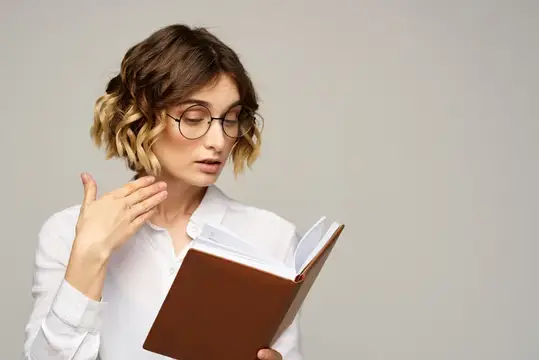 Молодая женщина в очках с книгой в руках на сером фоне