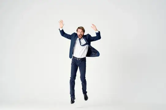 Мужчина в деловом костюме радостно подпрыгивает с поднятыми руками