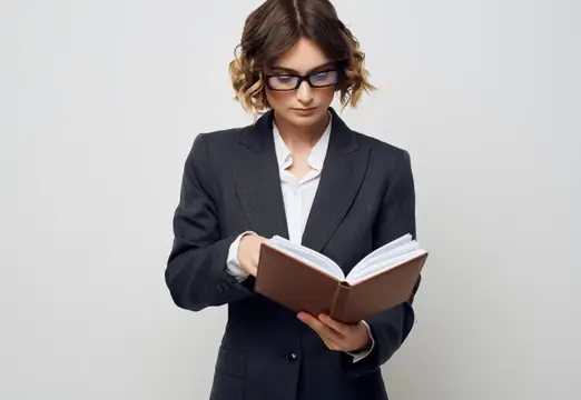 Молодая женщина в очках и деловом костюме читает книгу
