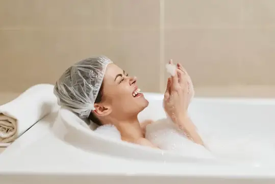 Улыбающаяся женщина в шапочке для душа нежится в пенной ванне