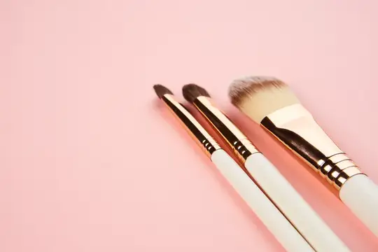 Три кисти для макияжа с золотистыми ручками на розовом фоне