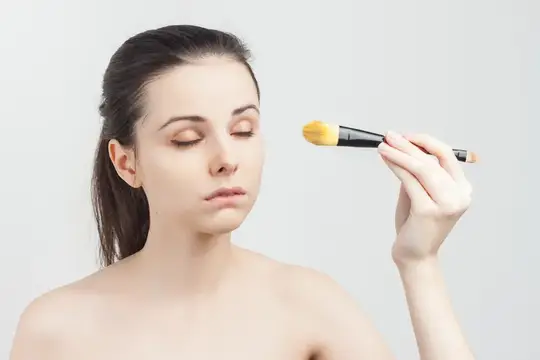 Молодая женщина с закрытыми глазами держит кисть для макияжа у лица