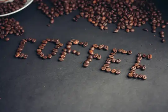 Слово coffee, выложенное кофейными зёрнами на тёмном столе